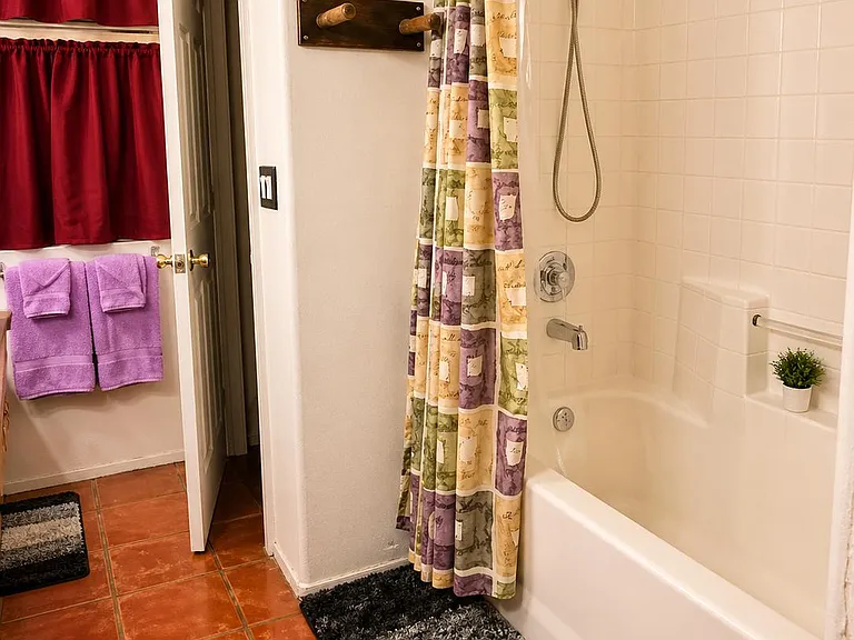 Full bath with tiled tub/shower combo, handheld showerhead, built-in ledge, and durable tile flooring with towel storage.