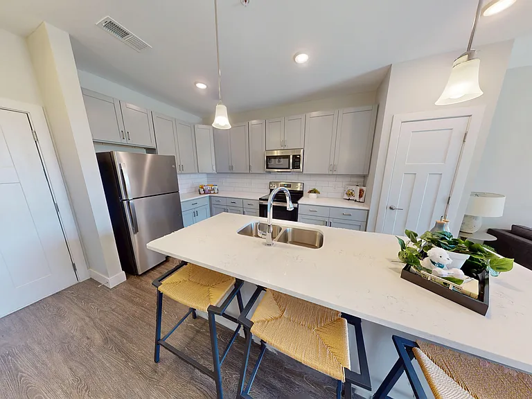 The Oak floor plan's kitchen features a large island, double sink, quartz countertops, a pantry, and stainless steel appliances. The Oak floor plan's kitchen features a large island, double sink, quartz countertops, a pantry, and stainless steel appliance