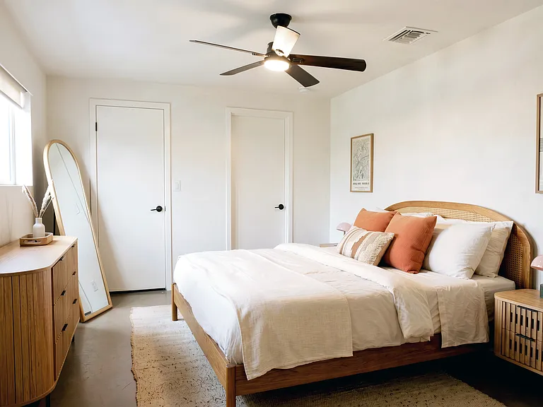 Bright bedroom with king bed, dresser, mirror, and ample storage.