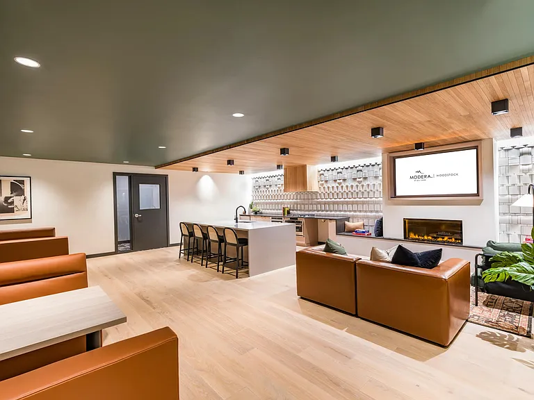 Relax in Modera Woodstock's stylish clubroom featuring a cozy fireplace and a sleek TV lounge for ultimate comfort.