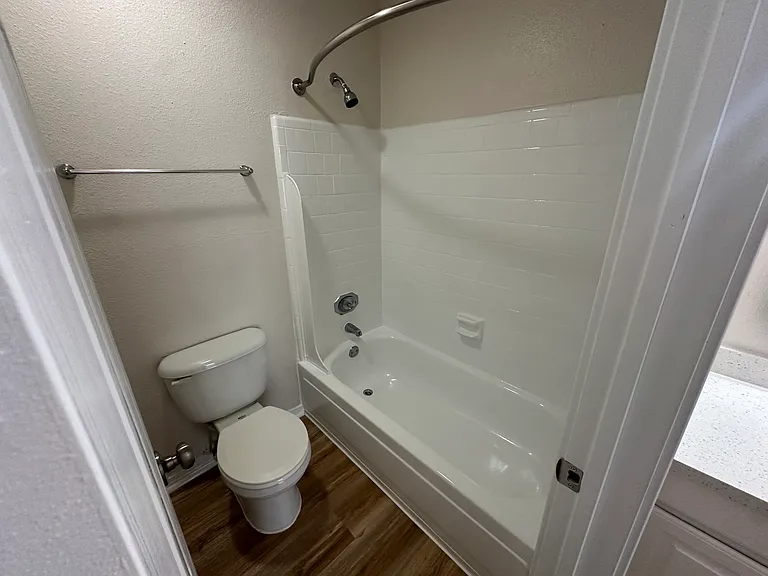 Modern bathroom featuring a sleek white shower-tub combo and elegant fixtures on wood-style flooring. Modern bathroom featuring a sleek white shower-tub combo and elegant fixtures on wood-style flooring.