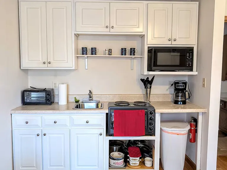 Compact kitchenette with ample cabinet storage, open shelving, and countertop appliances plus a convenient prep sink.