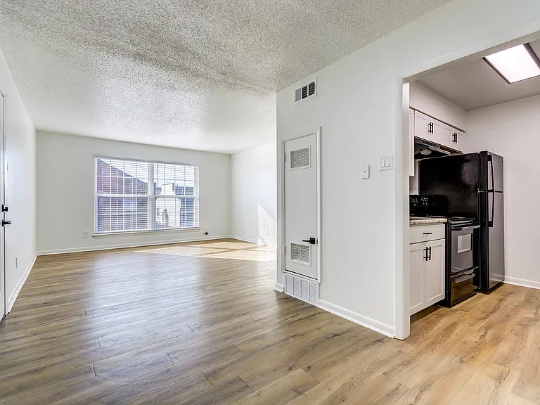 A newly renovated kitchen with black appliances is shown adjacent to an open-concept dining room overlooking a large living room at ReNew on Cantrell.