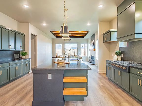 A kitchen with dark green cabinets, a central island featuring two open wooden shelves, and light wo