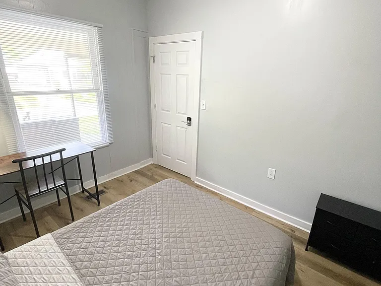 Private bedroom with a large window, wood-style flooring, and space for a bed plus a desk or dresser.