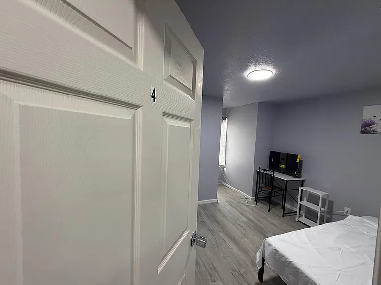 Private bedroom with wood-look flooring, a window for natural light, and space for a bed plus a small workstation/TV setup.