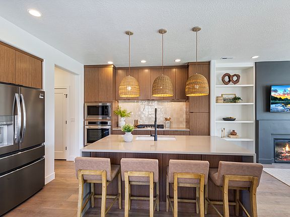 Modern kitchen with island, wooden bar stools, pendant lights, stainless steel appliances, and a coz