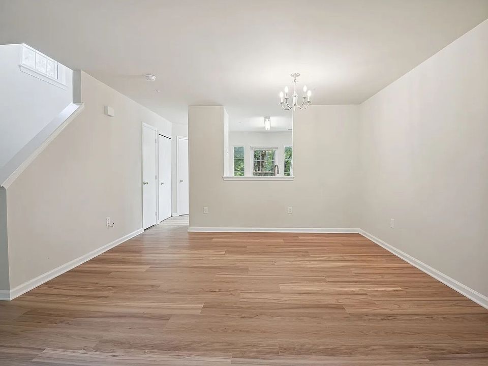 An overview of the living and dining area. The kitchen is visible beyond through the pass-through opening, while the coat closet, laundry closet, and half-bath doors are visible on the left along with the stairs to the upper level.