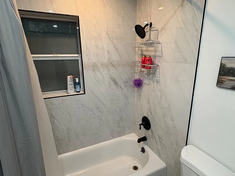 Updated tub/shower combo with marble-look wall tile, matte black fixtures, and a window for added ventilation.