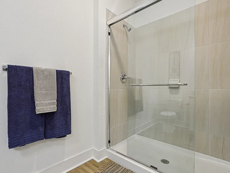 Contemporary bathroom featuring sleek glass shower doors, elegant tiles, and plush navy towels for a luxurious feel.