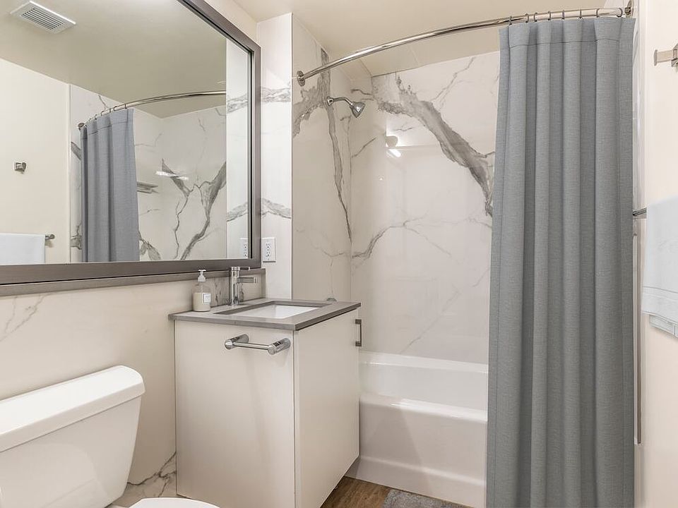 Renovated II North/South bath with grey quartz countertops, white lacquer cabinetry, marble surrounding, and hard surface flooring
