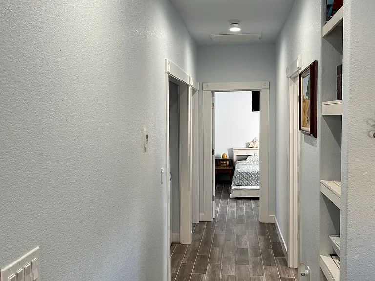 Hallway to the rooms in the house. Washer/dryer nook on the near left, book and printer shelves on the near right, half bathroom further along on the right, first bedroom on the far left and second bedroom at the end of the hall.
