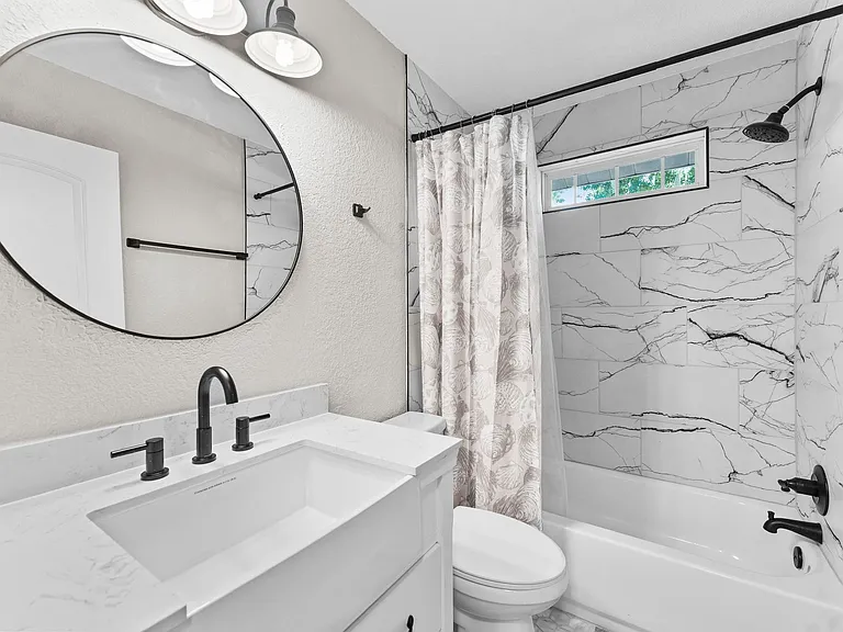 Updated full bath with a tub/shower combo, striking tile surround, wide vanity, and matte-black fixtures.