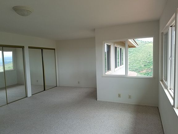 Standing at the same wall but in the other corner looking across the room. Behind the mirrored doors on the left is much closet space. Looking out the window, you see the windows of the other upstairs apartment.