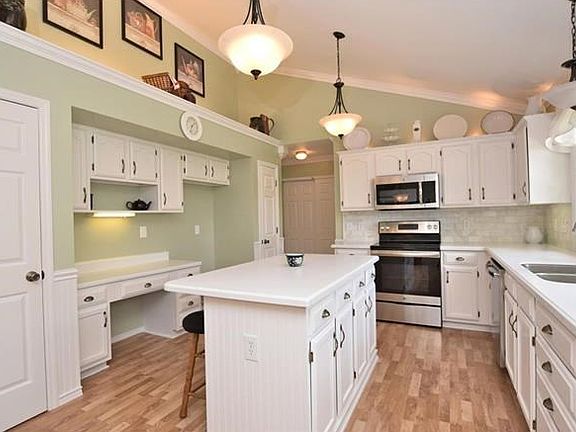 Cooks dream vaulted bright white kitchen with tons of professionally painted cabinets, stainless appliances, marble subway tile backsplash, silestone counters, laminate floor, 2 pantries, planning desk/coffee bar, display shelf & modern lighting