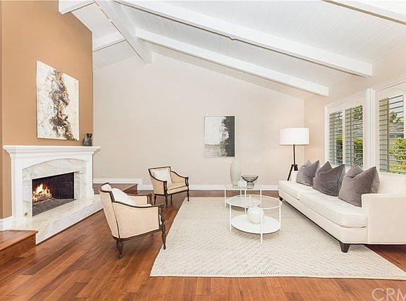 Formal living room with elegant marble fireplace, hardwood floors, plantation shutters and vaulted ceiling