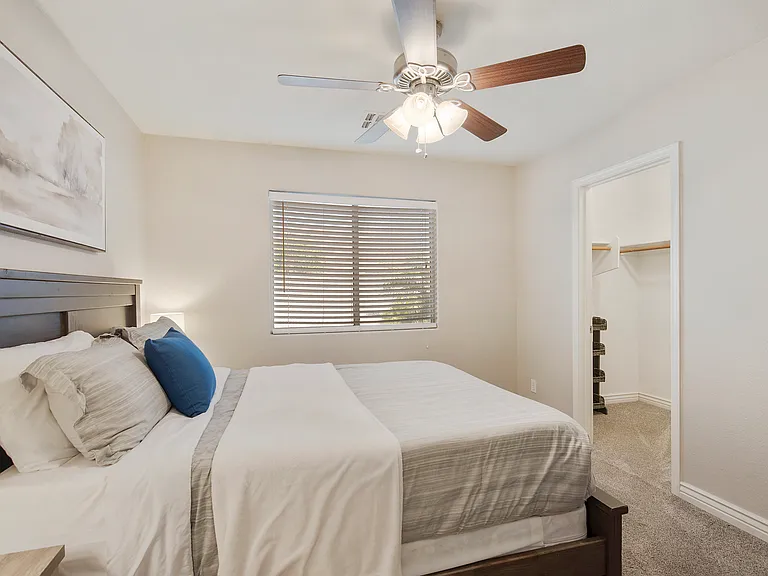 Bedroom 2 features a queen size bed, a dresser, 2 nightstands, a fan and a walk in closet