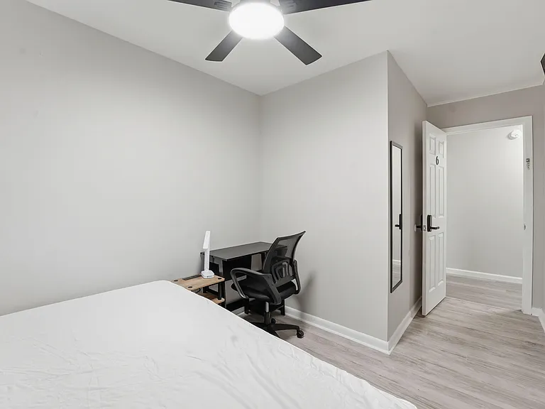 Private bedroom with ceiling fan, wood-look flooring, and space for a bed plus a work desk; convenient access to the hall.