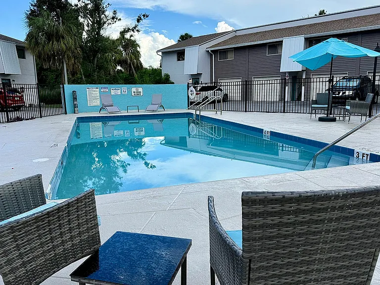 Inviting outdoor pool area with lounge chairs and a vibrant blue umbrella, perfect for relaxation and leisure in a serene community setting.