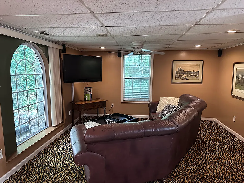 Living room showing leather sectional,large screen TV mounted on swivel stand. Lots of light shining through double payne windows. Artwork plentiful through out space.