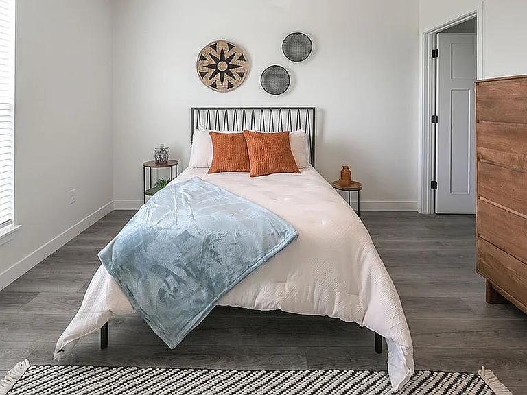 Inviting bedroom with modern decor, featuring a cozy bed with colorful pillows, elegant wall art, and abundant natural light from a large window.