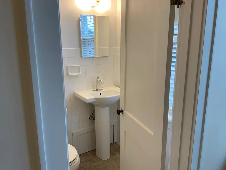 View into bathroom from living room. All white fixtures and walls. Bright, cheery and clean.