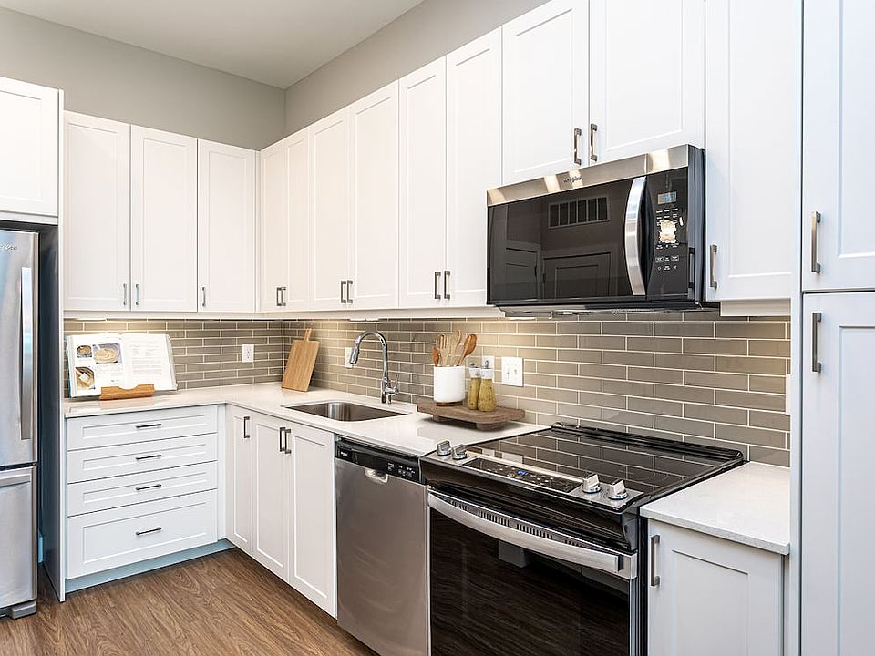 Modern kitchen with white cabinetry, undercabinet lighting, grey tile backsplash, and white quartz countertops
