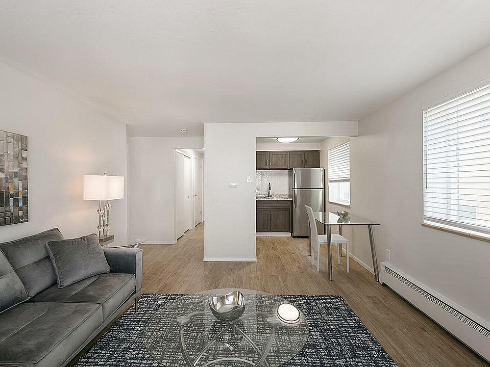 Modern open-concept living room with chic grey sofa, elegant glass coffee table, and cozy dining area next to a sleek kitchen featuring stainless steel appliances.
