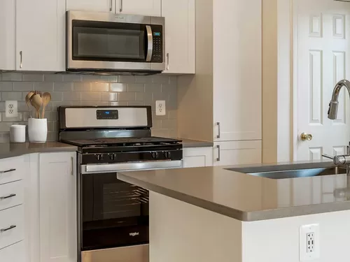 Renovated Package IV kitchens with white cabinetry, grey quartz countertops, stainless steel appliances, grey tile backsplash, and hard surface plank flooring - Avalon Tysons Corner