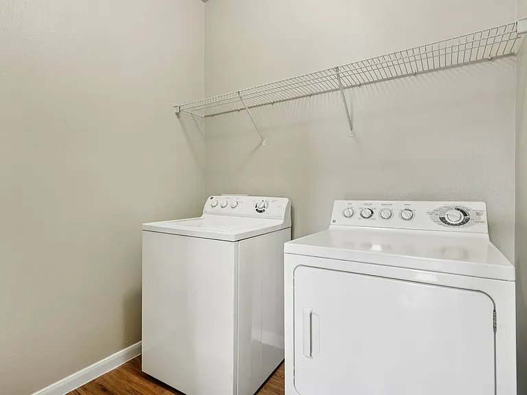 Modern laundry room with efficient white washer and dryer set, complemented by wood-style flooring and ample shelving. Modern laundry room with efficient white washer and dryer set, complemented by wood-style flooring and ample shelving.