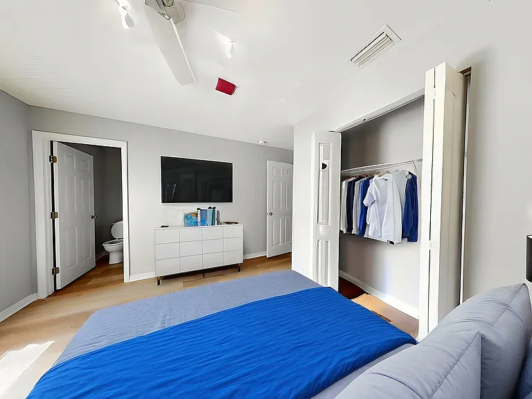 Bright and modern bedroom featuring a cozy bed with blue bedding, sleek white furniture, and ample closet space.