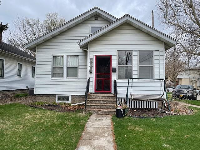 Front view of home. There is a swing in the front yard. Red screen door leads to the front porch.