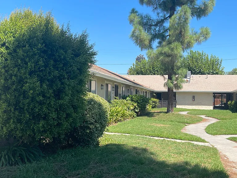 Mature Pine trees and established lawns at Eucalyptus Apartments in Moreno Valley, California.