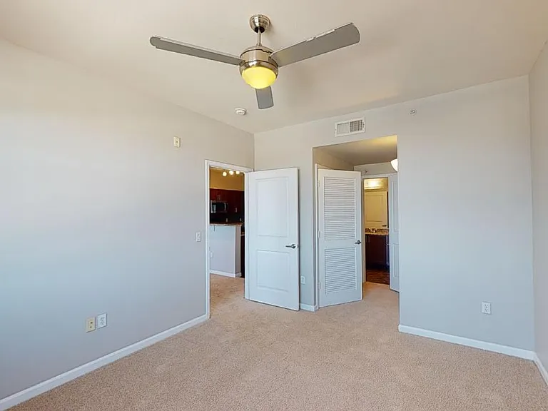 Spacious apartment bedroom with large closet, attached bathroom and plush carpet flooring.