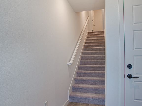 A staircase leading up to a second floor, with a white wall and a wooden floor visible in the foregr