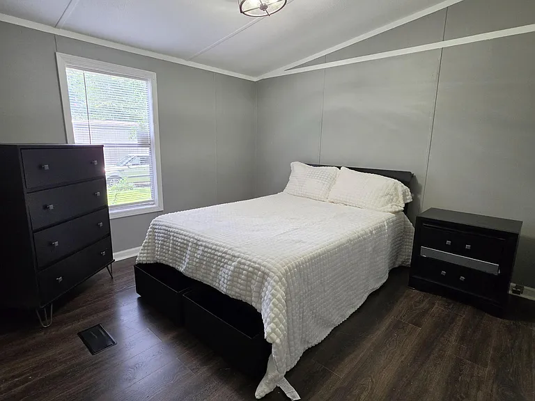 Furnished bedroom with a full bed, two dressers, and wood-look flooring, plus a window with blinds for natural light.