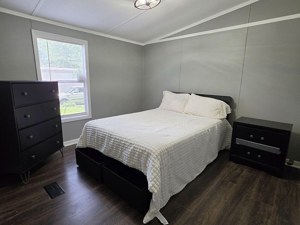 Furnished bedroom with a full bed, two dressers, and wood-look flooring, plus a window with blinds for natural light.