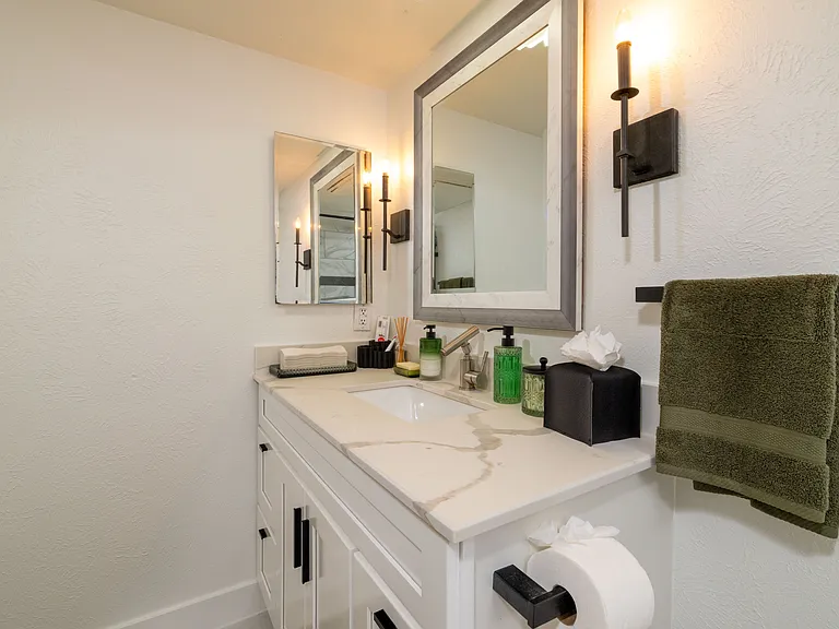This refreshed bathroom features a sleek vanity with soft lighting and a relaxing shower-tub combo with marble-style tile. Thoughtfully stocked with essentials for a comfortable and easy stay.