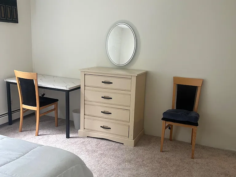 Carpeted bedroom with a furnished work area, dresser storage, and overhead ceiling fan for everyday comfort.
