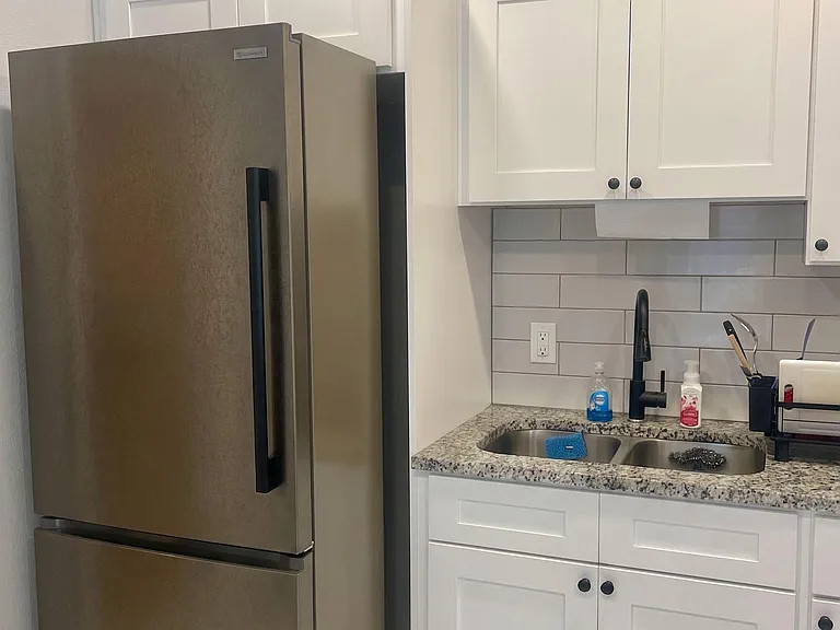 Efficient kitchen area with stainless-steel refrigerator, shaker cabinetry, granite-look counters, and a double-basin sink.