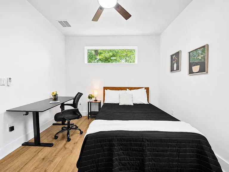 Private bedroom with a queen bed, dedicated work desk, ceiling fan, and high window providing natural light.