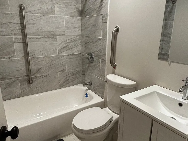Updated full bath with tiled tub/shower surround, safety grab bars, and a single-sink vanity with storage.