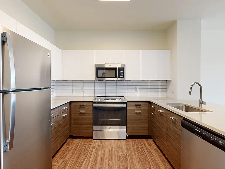 Apartment kitchen with stainless steel appliances, quartz countertops and wood-style flooring.
