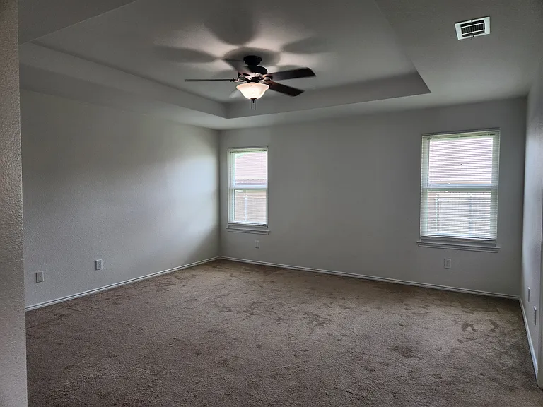 Primary bedroom has tray ceiling and ceiling fan