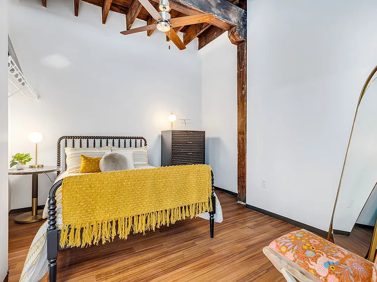 Whimsical Dreamscape: A bedroom sanctuary showcasing a unique metal-framed bed, adorned with vibrant yellow textures, and framed by rustic wooden architectural elements.