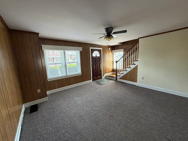 View of living room and front entrance door, with new ceiling fan, new mini blinds throughout the house.