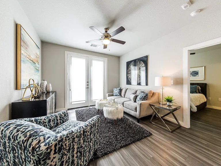 Living room with wood-style flooring, balcony/patio access, ceiling fan, with doorway to bedroom