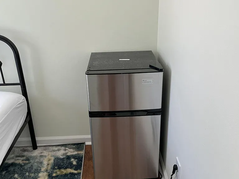 Private bedroom includes a convenient mini fridge for snacks and drinks, set on durable flooring with nearby outlet access.