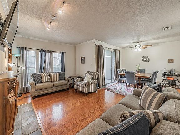 Living room featuring rail lighting, ceiling fan, ornamental molding, light hardwood / wood-style floors, and a textured ceiling