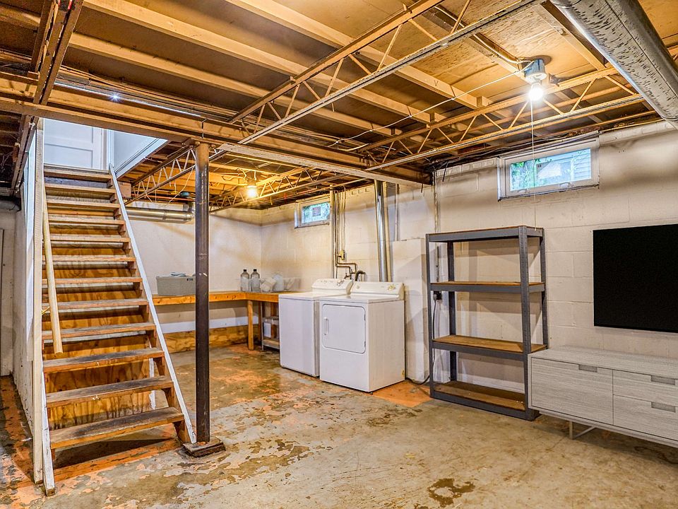 A basement with a wooden staircase, washing machine, countertop, and shelving unit against the wall.